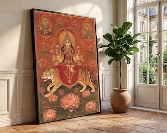 Könnte beinhalten: Gerahmtes Kunstwerk, das eine Gottheit zeigt, die auf einem Tiger sitzt, umgeben von Lotusblumen und Figuren. Das Kunstwerk verwendet eine rote und orange Farbpalette mit goldenen Akzenten. Die gerahmte Kunst wird vor einer weißen Wand ausgestellt.