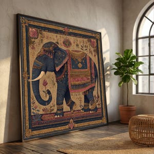 May include: A framed artwork featuring a detailed illustration of an elephant. The elephant is adorned with ornate blue and pink decorative elements. The artwork has a gold border and is set against a beige background with floral patterns. The artwork is leaning against a wall.