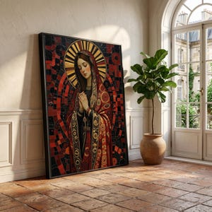 Puede incluir: Obra de arte enmarcada que representa una figura religiosa con un halo dorado y una túnica roja y dorada. La obra de arte está apoyada contra una pared blanca, con una planta en maceta y una ventana en el fondo. La obra tiene un marco negro.