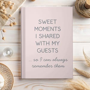 May include: A light pink journal with the text "SWEET MOMENTS I SHARED WITH MY GUESTS ... so I can always remember them" in gray lettering. The journal is on a light wood surface with decorative elements.