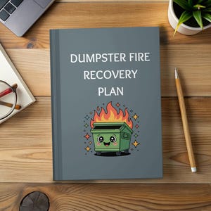 May include: A gray notebook with the text "DUMPSTER FIRE RECOVERY PLAN" and a cartoon dumpster on fire. The dumpster is green with a smiling face, flames, and star accents. The notebook is on a wooden surface.