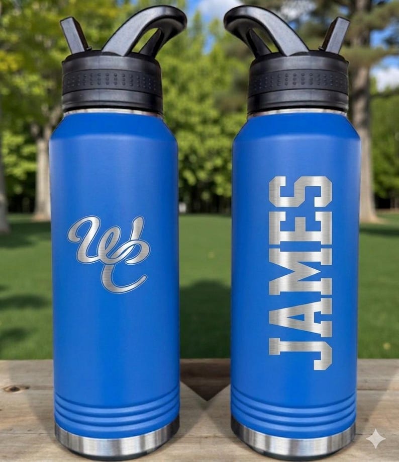 May include: Two blue water bottles with black lids and silver accents. One bottle has the name "JAMES" in silver block letters. The other bottle has a silver "Wb" logo. Both bottles are on a wooden surface.