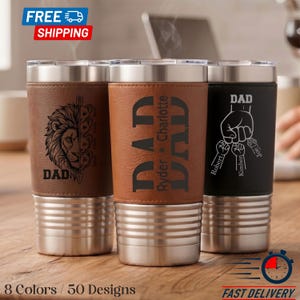 May include: Three personalized travel mugs with stainless steel bases and leather sleeves. One features a lion design, another has "DAD" and names, and the third has a hand holding keys with names. The mugs are in brown and black.
