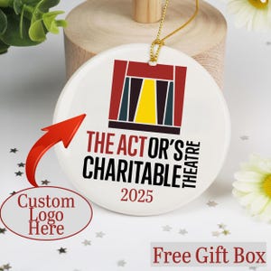 May include: White ceramic ornament with a gold string for hanging. The ornament features a logo with red, yellow, and blue colors, along with the text "THE ACTOR'S CHARITABLE THEATRE 2025". A red arrow points to a text bubble that says "Custom Logo Here".