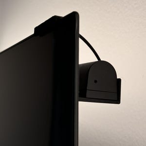Può includere: Una webcam nera montata sul bordo superiore di uno schermo televisivo nero.