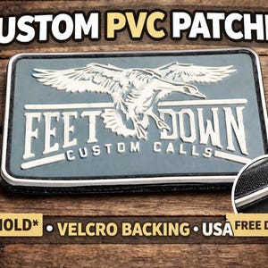 Puede incluir: Parche de PVC personalizado con un diseño de pato en vuelo y el texto "FEET DOWN CUSTOM CALLS". El parche es gris, blanco y negro, con las palabras "CUSTOM PVC PATCHES" en la parte superior. El parche tiene respaldo de velcro.