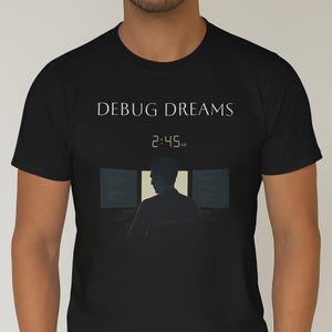 Puede incluir: Camiseta negra con la frase "DEBUG DREAMS" y la hora 2:45 AM. El diseño muestra la silueta de una persona frente a tres pantallas de ordenador, sugiriendo trabajo nocturno.