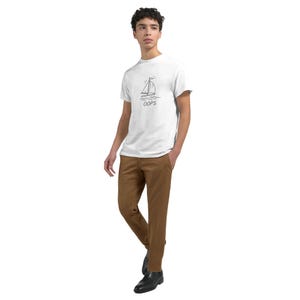 Peut inclure: Un t-shirt blanc avec un dessin de voilier et le mot "OOPS" en noir. La personne porte un pantalon marron et des chaussures noires. Le t-shirt est de style décontracté.