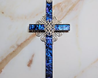 May include: A silver and blue cross with a decorative filigree design. The cross is made of iridescent abalone shell.