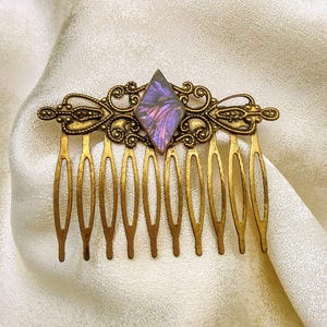 May include: A gold hair comb with a decorative design and a purple iridescent gemstone in the center.