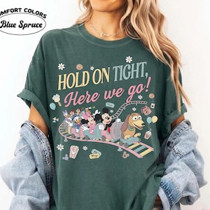 May include: Dark green t-shirt with the text "HOLD ON TIGHT, Here we go!" and a cartoon roller coaster design featuring Mickey Mouse, Donald Duck, and other characters. The shirt is labeled "Comfort Colors Blue Spruce".