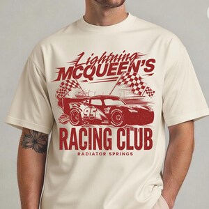 May include: Cream-colored t-shirt featuring a red graphic of Lightning McQueen's race car, the number 95, and checkered flags. The text reads "Lightning McQueen's Racing Club" and "Radiator Springs".