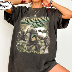 May include: Dark gray Comfort Colors t-shirt featuring a graphic from The Mandalorian and Grogu. The design includes the Mandalorian, Grogu, and text that reads "This is the Way". The shirt also has the text "COMIC DESIGNS" and "Pepper" on it.