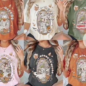 Puede incluir: Una colecci&oacute;n de seis camisetas de manga corta en varios colores, cada una con un estampado gr&aacute;fico de un personaje de dibujos animados con disfraz de Halloween, incluyendo momias y un coche de carreras, rodeados de dulces y calabazas.