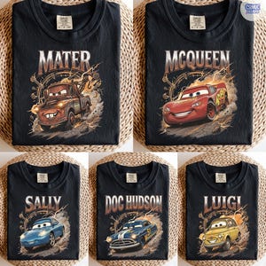 Pode incluir: Camisetas pretas com personagens do filme de anima&ccedil;&atilde;o Carros. Cada camisa exibe o nome de um personagem diferente em uma fonte vintage, junto com uma ilustra&ccedil;&atilde;o do personagem. Os personagens incluem Mater, McQueen, Sally, Doc Hudson e Luigi.