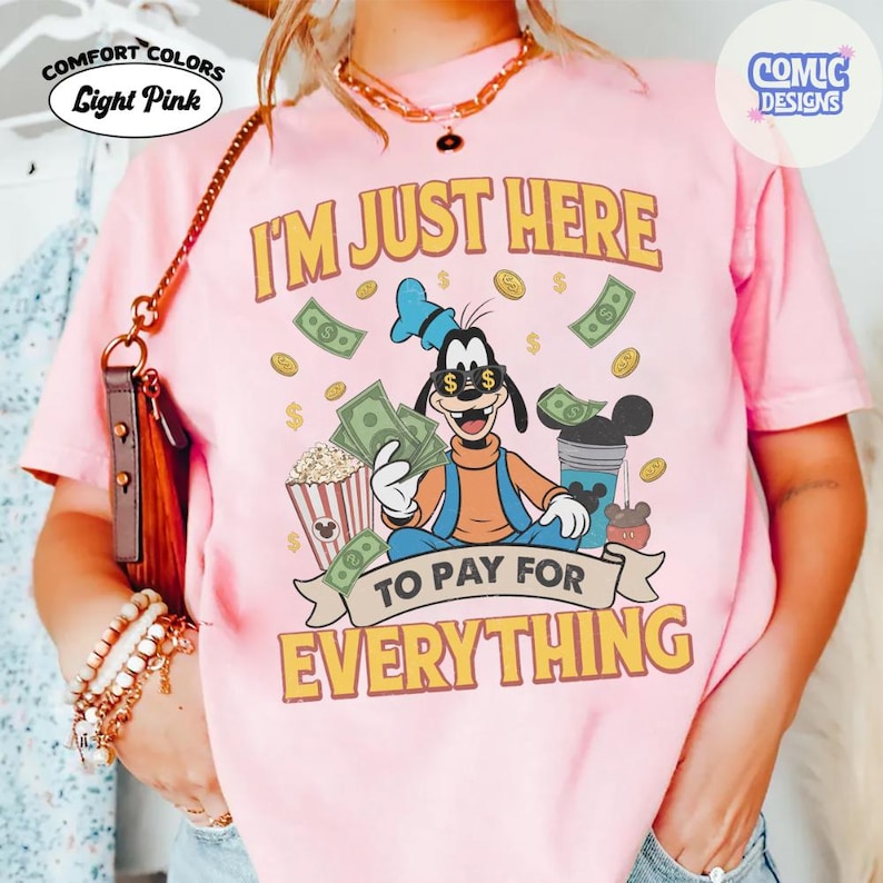 May include: Light pink Comfort Colors t-shirt with the text "I'M JUST HERE TO PAY FOR EVERYTHING". The graphic features a cartoon character holding money and popcorn, with dollar signs and coins.