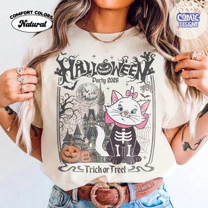 Puede incluir: Una camiseta de color natural con un estampado gr&aacute;fico que incluye el texto Halloween Party 2026 y Trick or Treet. El dise&ntilde;o muestra un gato blanco con un lazo rosa y caja tor&aacute;cica de esqueleto, un castillo, luna llena y calabazas.