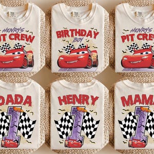 Puede incluir: Seis camisetas de color blanco roto con estampados gr&aacute;ficos en rojo y negro. Los dise&ntilde;os incluyen un coche de carreras rojo, banderas a cuadros, telara&ntilde;as y murci&eacute;lagos. El texto incluye Henry's Pit Crew, Birthday Boy, Dada, Henry, Mama y el n&uacute;mero uno.