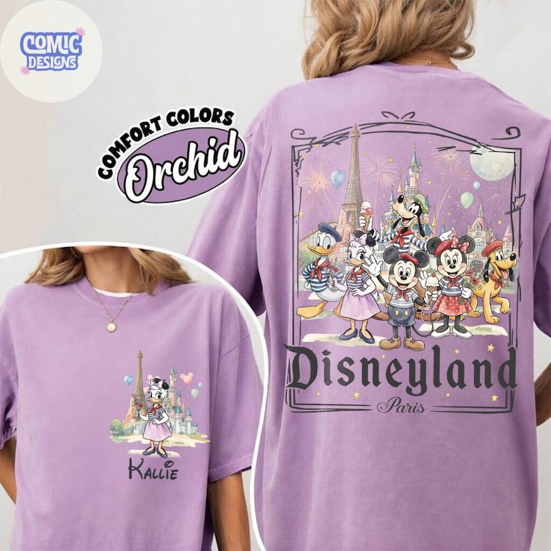 May include: An orchid-colored t-shirt featuring a graphic of Daisy Duck in front of a castle on the front, and a large back graphic of Mickey Mouse, Minnie Mouse, Donald Duck, Daisy Duck, Goofy, and Pluto at Disneyland Paris with text.