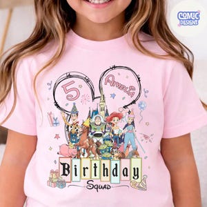 May include: Pink t-shirt featuring a colorful graphic of Toy Story characters, the number 5, and the name Amelia. The words "Birthday Squad" are also displayed. The design is set within a Mickey Mouse ear outline.