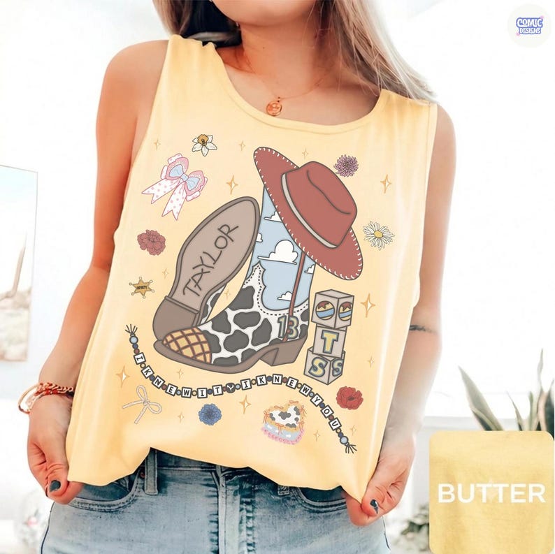 Puede incluir: Una camiseta sin mangas de color amarillo p&aacute;lido con un estampado gr&aacute;fico de una bota de vaquero con manchas de vaca, un sombrero de vaquero marr&oacute;n, un collar de cuentas con el texto I KNEW YOU WERE TROUBLE y bloques con las letras T S.
