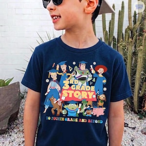 May include: Navy blue t-shirt featuring a colorful graphic of Toy Story characters wearing graduation caps. The text reads "3rd Grade Story" and "To Fourth Grade and Beyond".