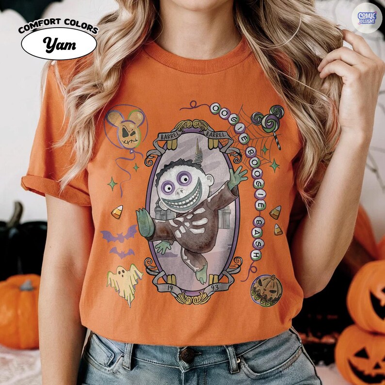 Puede incluir: Una camiseta naranja de manga corta con un gr&aacute;fico del personaje Barrel de Pesadilla antes de Navidad dentro de un marco ovalado ornamentado. El dise&ntilde;o incluye el texto OOGIE BOOGIE BASH, un fantasma, murci&eacute;lagos, ma&iacute;z dulce y una calabaza.