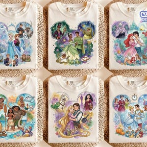 May include: A collection of six off-white t-shirts featuring watercolour-style illustrations of Disney characters arranged in Mickey Mouse ear shapes. Each shirt displays scenes from movies like Frozen, The Princess and the Frog, The Little Mermaid, Moana, Tangled, and Cinderella, with the text Comic Designs in the top right corner.