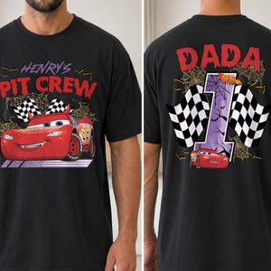Puede incluir: Una camiseta negra con un gr&aacute;fico de coche de carreras rojo en la parte delantera con el texto "HENRY'S PIT CREW" y detalles de telara&ntilde;as. La parte trasera muestra un n&uacute;mero uno grande, el texto "DADA", banderas a cuadros y un coche rojo.
