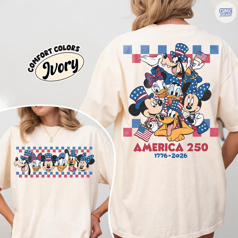 May include: Ivory-colored t-shirt featuring a graphic of Disney characters in patriotic attire, including Mickey and Minnie Mouse, Donald and Daisy Duck, and Pluto. The shirt has the text "AMERICA 250 1776-2026" and a Comfort Colors label.