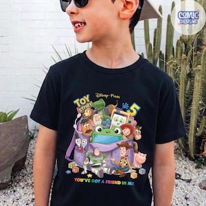 May include: A black t-shirt featuring a colourful graphic of Toy Story characters emerging from a purple backpack. The design includes Buzz Lightyear, Woody, Rex, and other figures, with the text Toy Story 5 and You've Got a Friend in Me.