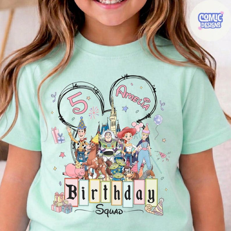 May include: A light green t-shirt featuring a colorful graphic of Disney's Toy Story characters. The design includes the text "Birthday Squad" and the name "Amelia" with the number "5". The shirt has short sleeves and a round neckline.