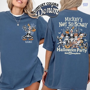Puede incluir: Camiseta azul denim con dise&ntilde;o de Halloween. La parte delantera muestra un Goofy esqueleto de dibujos animados con una calabaza y la palabra "NAME". La parte trasera presenta a Mickey Mouse y sus amigos como esqueletos, con el texto "Mickey's Not So Scary Halloween Party".