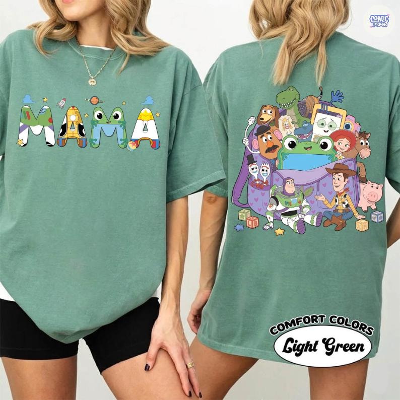 May include: A sage green t-shirt featuring the word MAMA on the front, with each letter styled after Toy Story characters. The back displays a purple backpack filled with various Toy Story characters, including Buzz Lightyear, Woody, and Rex.