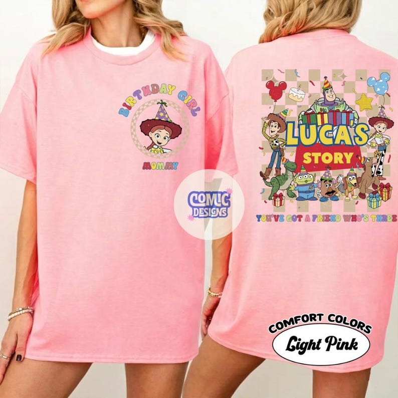 May include: Pale pink t-shirt with a cartoon graphic and the words "BIRTHDAY GIRL" on the front. The back of the shirt shows "LUCAS STORY" with cartoon characters and the phrase "YOU'VE GOT A FRIEND IN ME".
