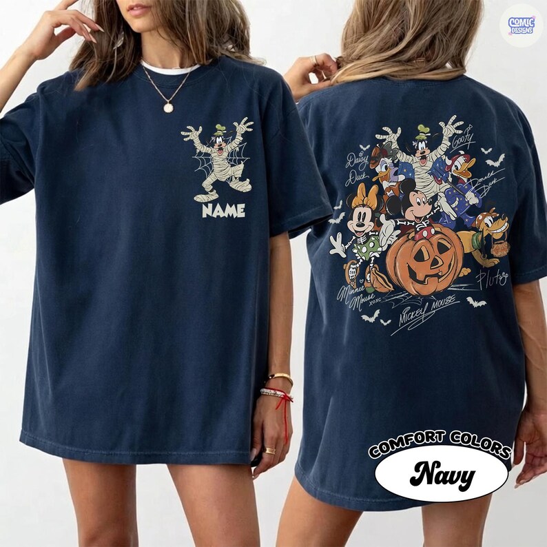 May include: A navy blue t-shirt featuring a graphic of Goofy dressed as a mummy on the front chest above the word NAME. The back displays a large Halloween-themed illustration of Mickey Mouse, Minnie Mouse, Donald Duck, Daisy Duck, Goofy, and Pluto.