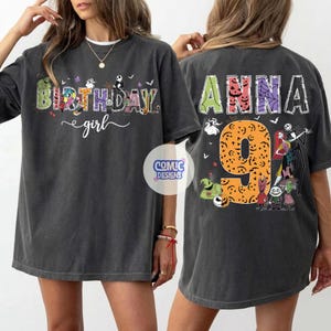 May include: A charcoal gray t-shirt featuring a front graphic with the text BIRTHDAY girl and characters from The Nightmare Before Christmas. The back displays the name ANNA, the number 9, and various characters from the same movie.