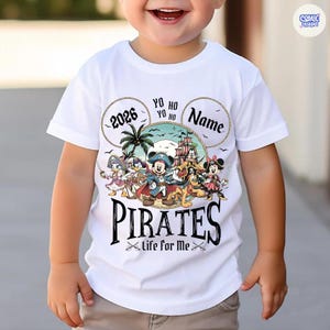May include: White t-shirt featuring a colorful graphic of Disney characters dressed as pirates. The design includes the word "PIRATES" in a bold font, the year "2026", and the phrase "Life for Me". The shirt has a round neckline and short sleeves.
