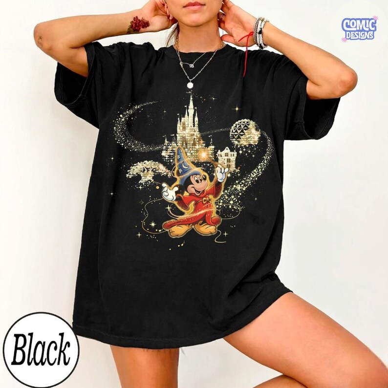 May include: Black t-shirt featuring a graphic of Mickey Mouse as a sorcerer in red and gold attire, with a castle and sparkling accents. The text "COMIC DESIGNS" is in the upper right corner, and "Black" is in a circle at the bottom.