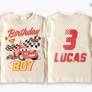 Puede incluir: Camiseta color crema con tem&aacute;tica de cumplea&ntilde;os. La parte delantera muestra la palabra "Birthday" en rosa, un coche de dibujos animados y la palabra "BOY" en amarillo. La parte trasera muestra el n&uacute;mero "3" y el nombre "LUCAS" en rojo.