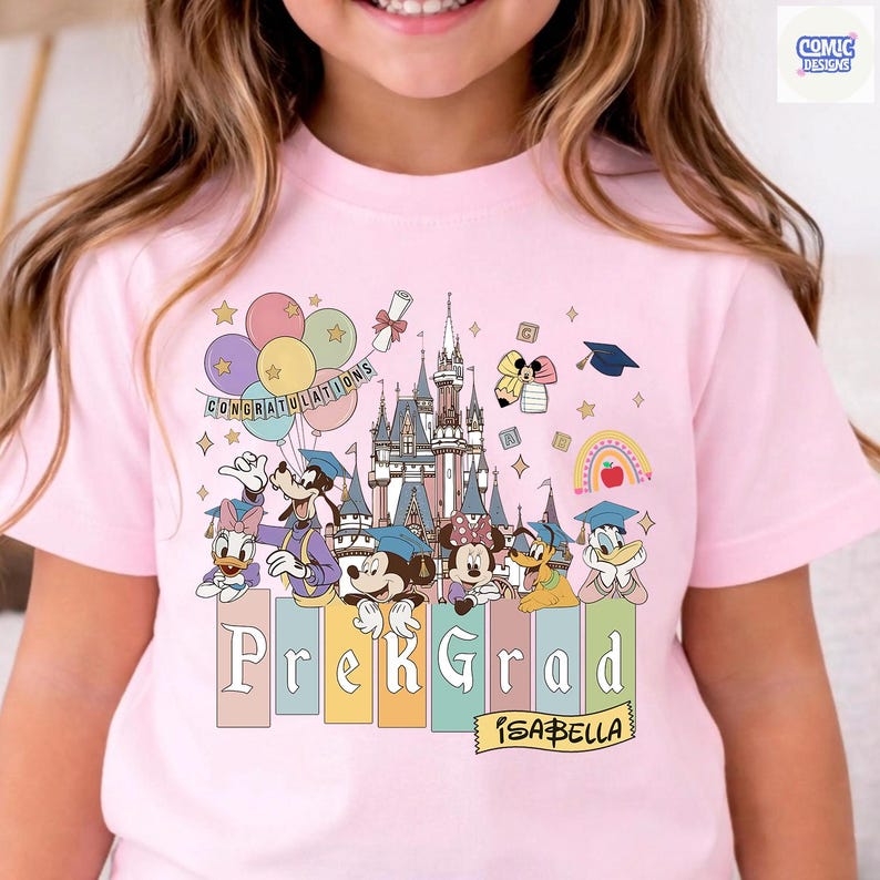May include: Pink t-shirt featuring a colorful graphic of Disney characters celebrating a Pre-K graduation. The design includes a castle, balloons, and the text "Prek Grad" with the name "Isabella".