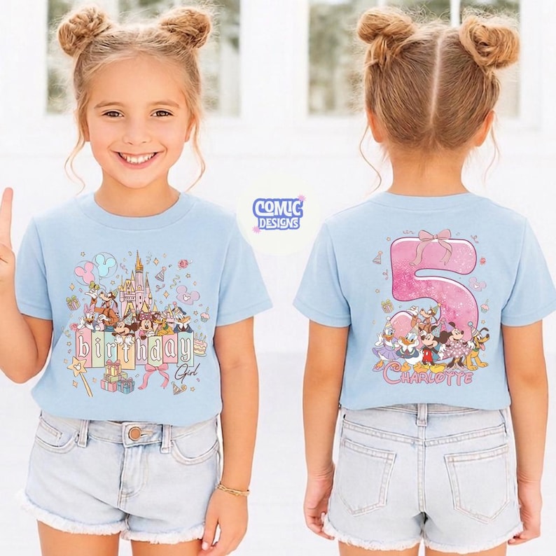 May include: A light blue t-shirt featuring a colorful graphic of a castle, characters, and the text "Birthday Girl". The back of the shirt displays a large pink number 5 with characters and the name "Charlotte".