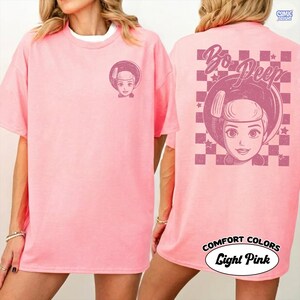 Puede incluir: Camiseta rosa claro con un dise&ntilde;o de Bo Peep en la parte delantera y trasera. La parte delantera tiene una peque&ntilde;a imagen de Bo Peep, mientras que la parte trasera muestra una imagen m&aacute;s grande dentro de un patr&oacute;n de cuadros, con el texto "Bo Peep". La camiseta est&aacute; etiquetada como "Comfort Colors Light Pink".