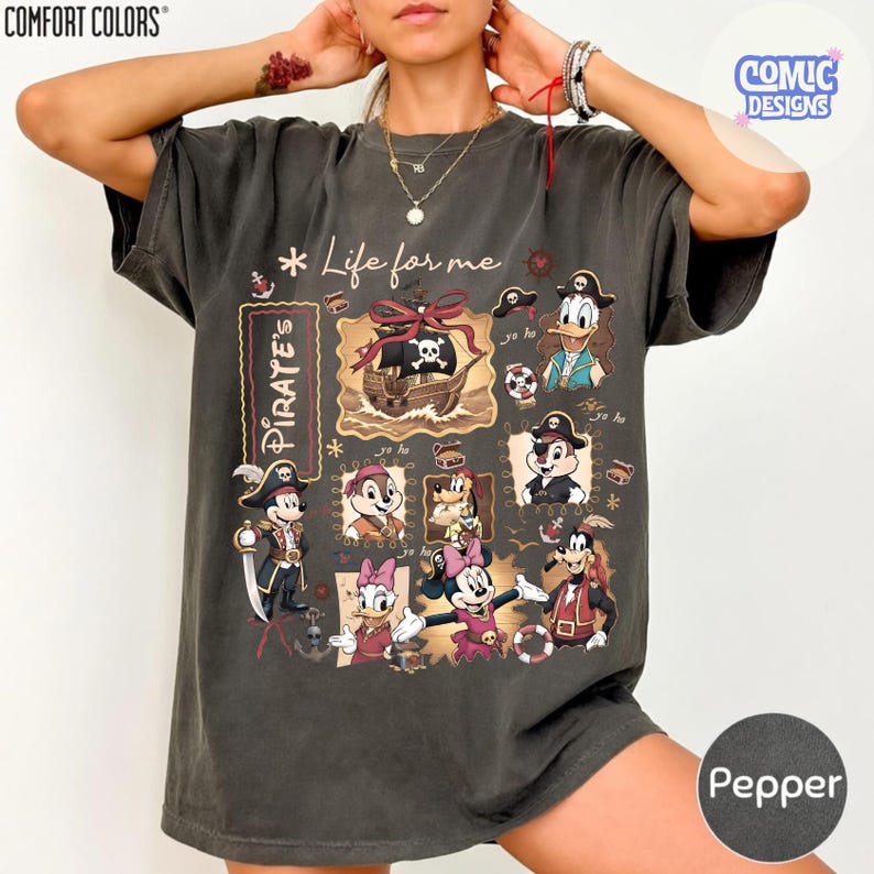 May include: Pepper-colored t-shirt featuring a pirate-themed graphic with various cartoon characters. The design includes a pirate ship, skull and crossbones, and the text "Life for me" and "Pirate's". The shirt is from Comfort Colors.
