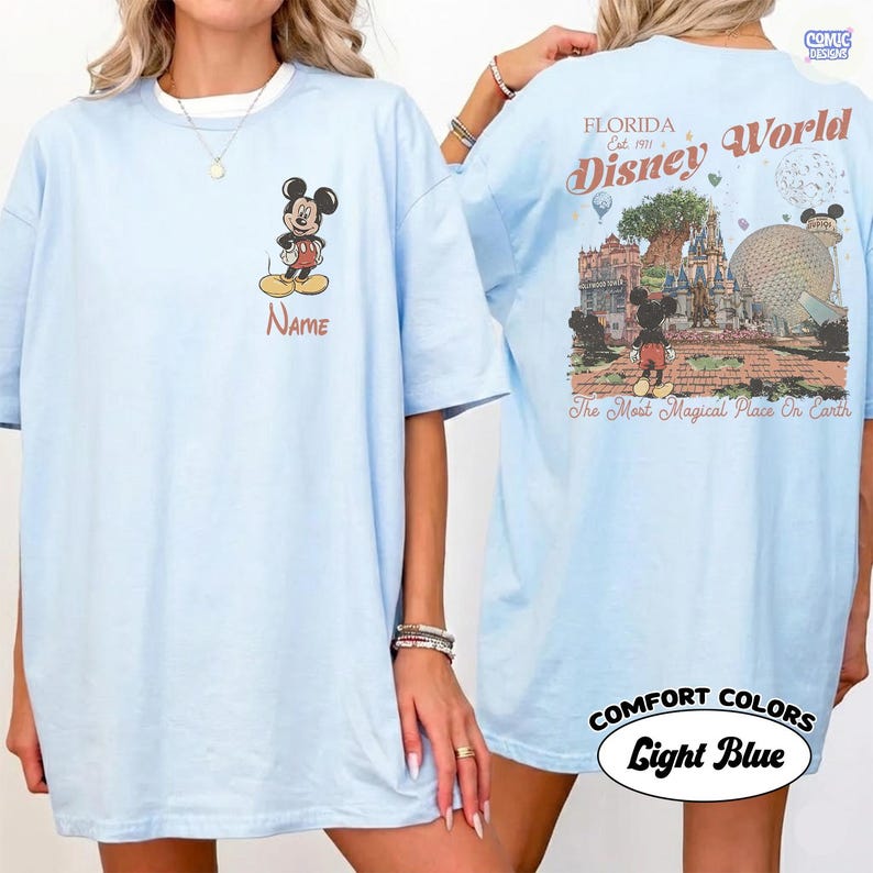 K&ouml;nnte beinhalten: Hellblaues T-Shirt mit Mickey Mouse auf der Vorderseite und dem Namen "Name" darunter. Auf der R&uuml;ckseite befindet sich ein "Florida Disney World"-Design mit Parkbildern und dem Text "The Most Magical Place On Earth."