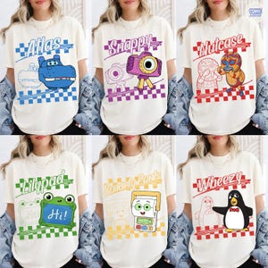 May include: A collection of six off-white t-shirts featuring cartoon characters and names: Atlas with a blue hippo, Snappy with a purple camera, Nutcase with a wrestler, Lilypad with a green frog, Smarty Pants with a calculator, and Wheezy with a penguin.