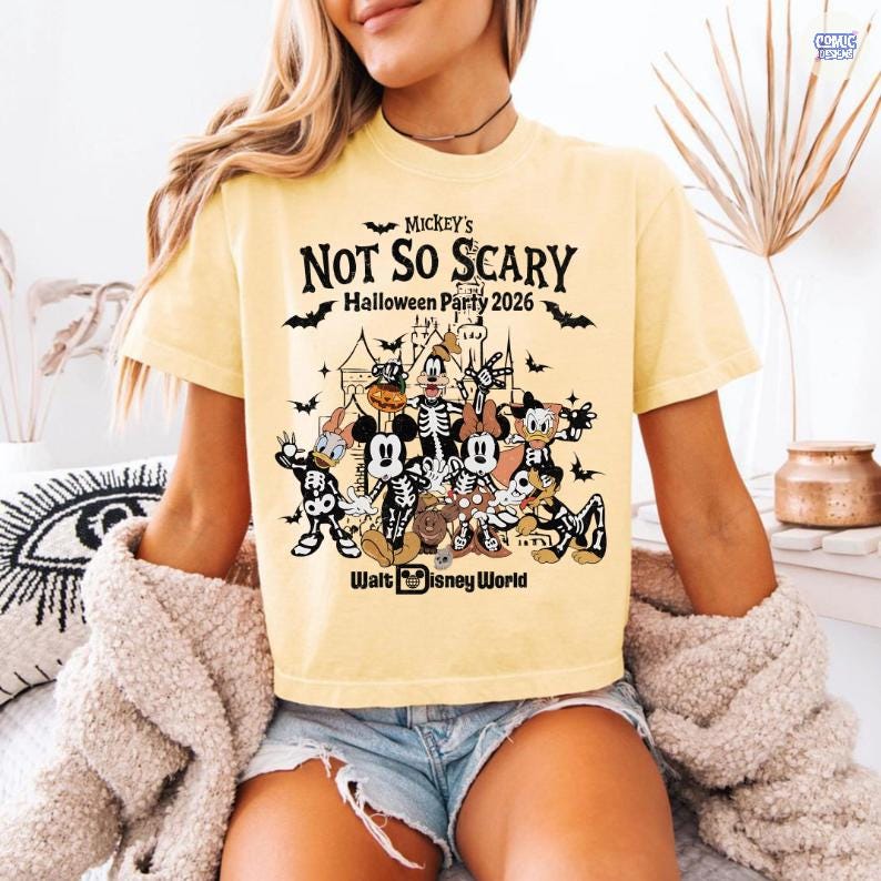 May include: A light yellow t-shirt featuring a graphic for Mickey's Not So Scary Halloween Party 2026 at Walt Disney World. The graphic includes Disney characters in skeleton costumes, bats, and a castle.
