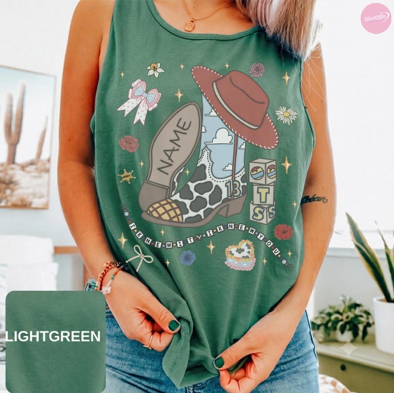 Puede incluir: Una camiseta sin mangas de color verde claro con un estampado gr&aacute;fico de una bota de vaquero con patr&oacute;n de manchas de vaca, un sombrero marr&oacute;n, un lazo y bloques. El texto "NAME" aparece en la bota y "I KNEW IT I KNEW YOU" debajo.