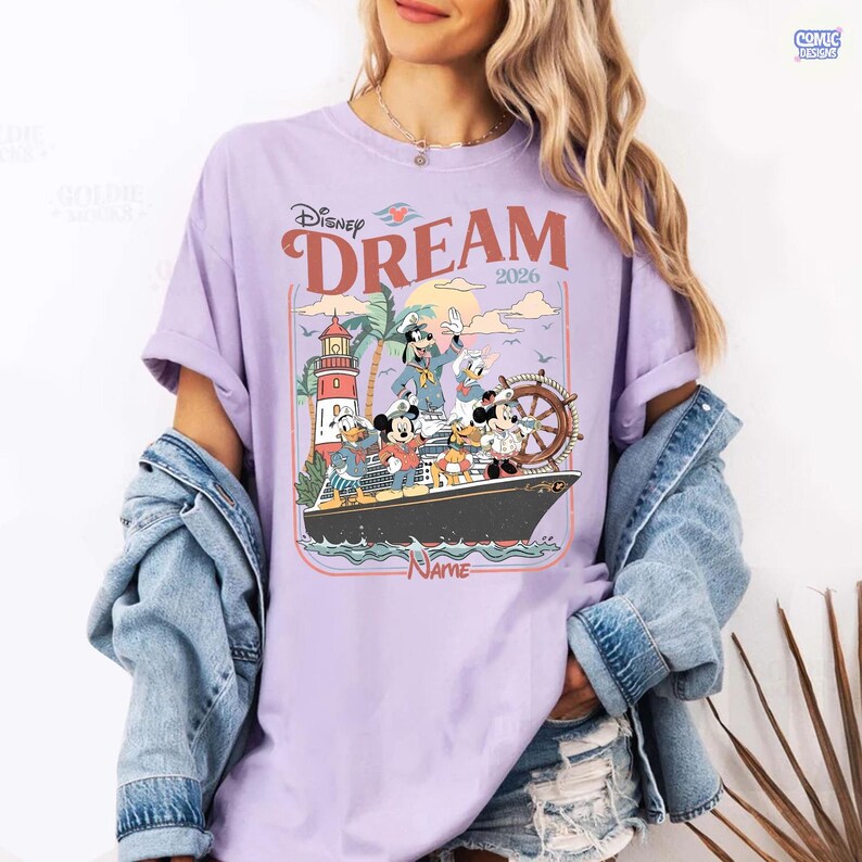 Puede incluir: Una camiseta de color lila claro con un dise&ntilde;o de personajes de Disney en un crucero. El dise&ntilde;o incluye las palabras "Disney Dream 2026" y un faro. La camiseta tiene las mangas dobladas.