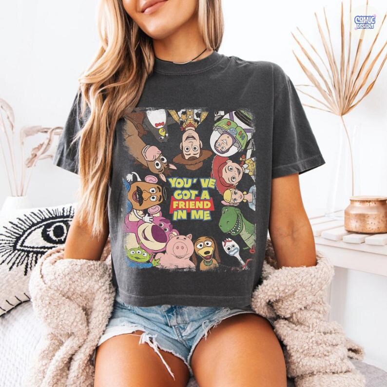 May include: Dark gray t-shirt featuring a colorful graphic of characters from the animated movie Toy Story. The graphic includes Woody, Buzz Lightyear, and other characters, with the text "YOU'VE GOT A FRIEND IN ME".